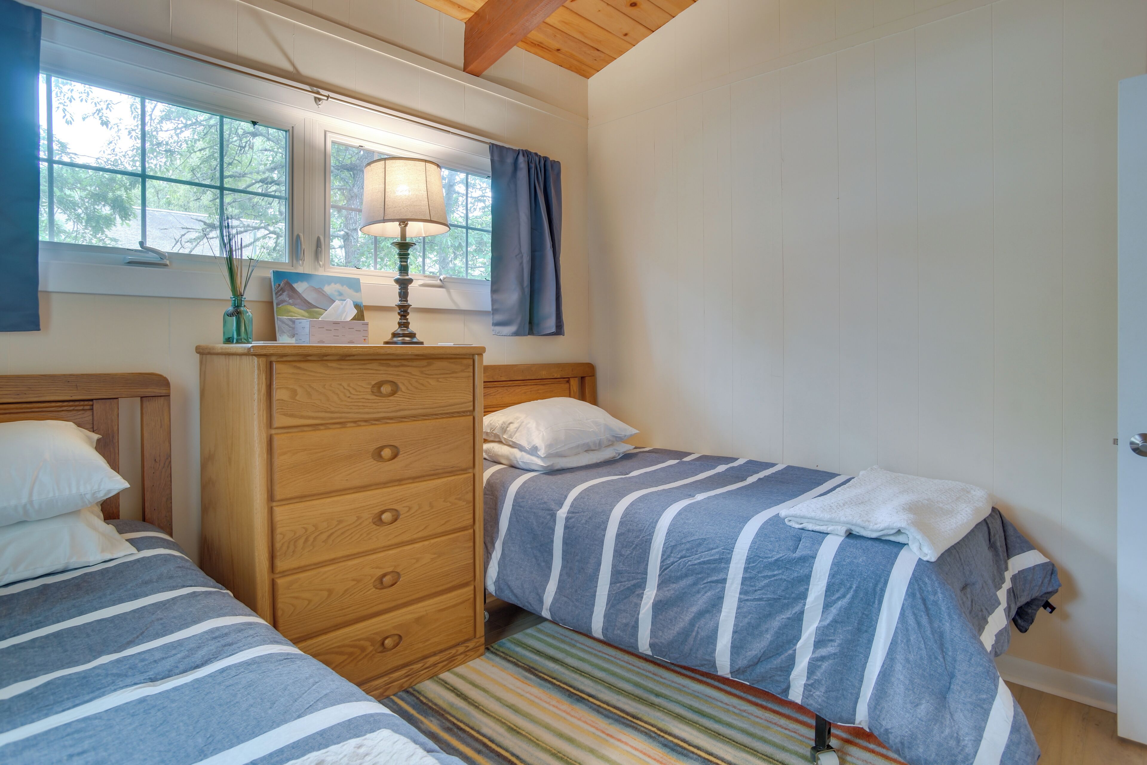 Un dormitorio con dos camas, un aparador de madera, una lámpara y una ventana con cortinas.
