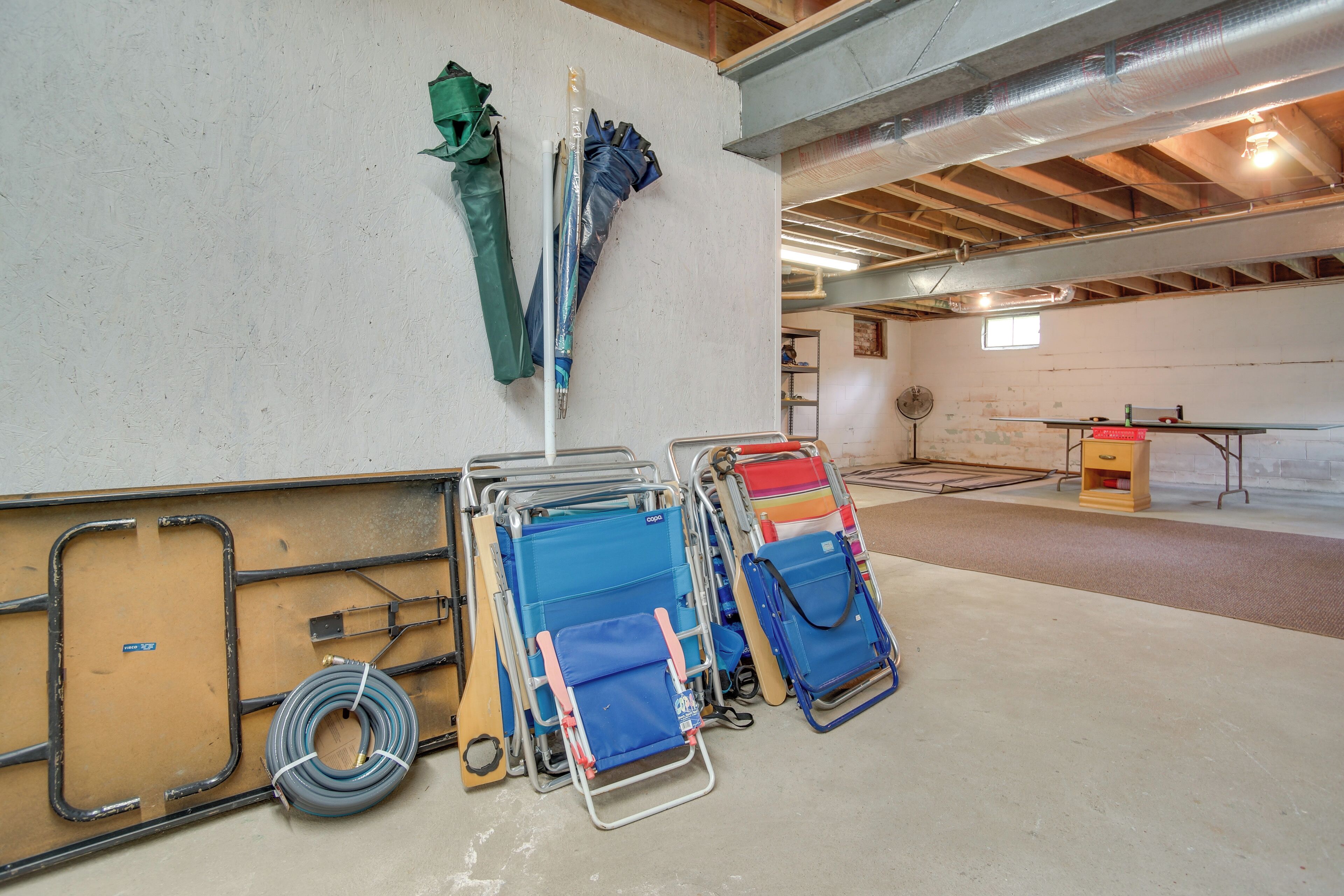 Un espace de stockage équipé d’étagères métalliques où sont rangés divers objets, notamment des sacs bleus et rouges, ainsi qu’un tuyau enroulé sur le sol.