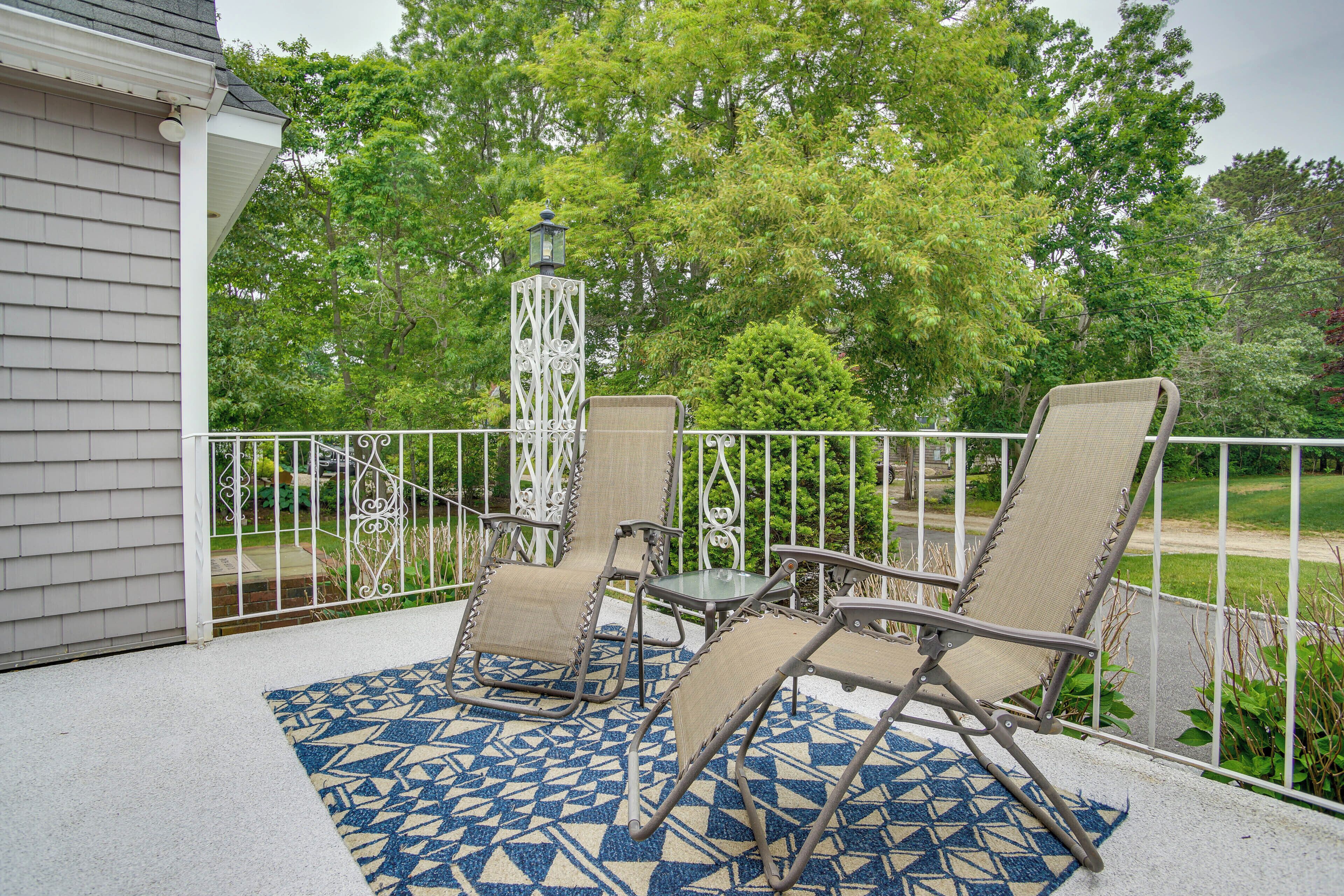 A covered patio with two chairs and a table, a decorative lantern, and a patterned rug.