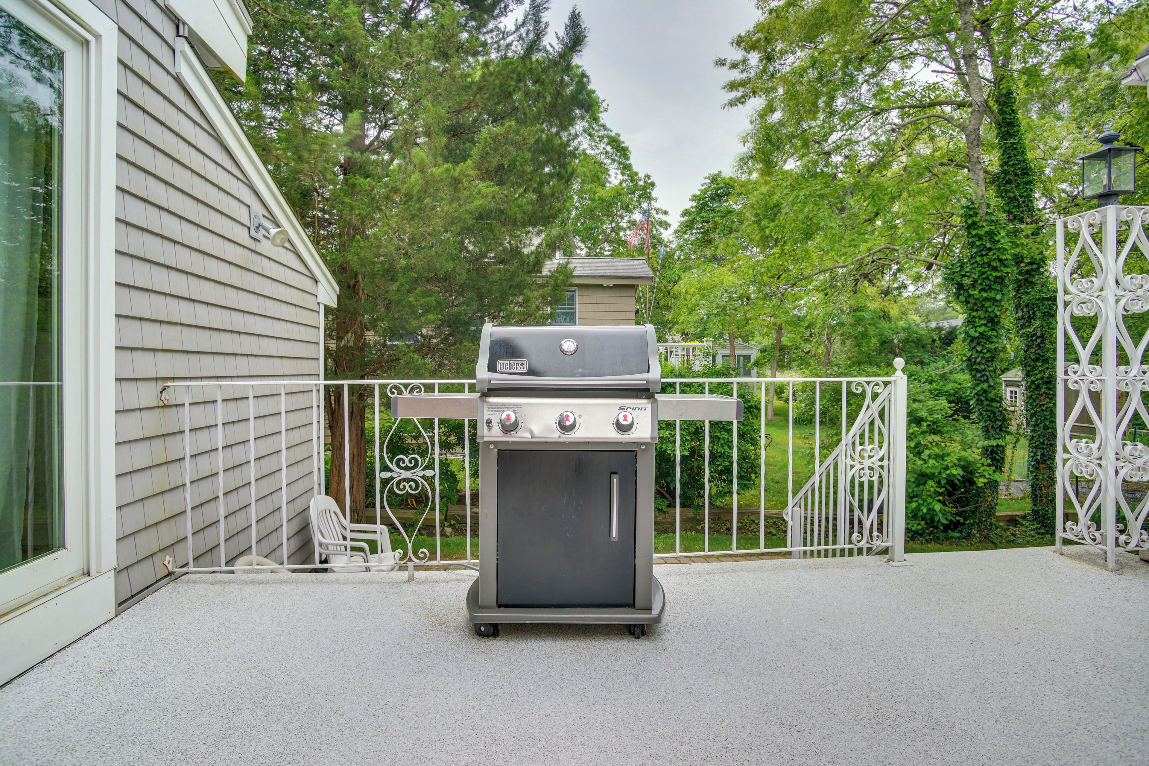 Un barbecue portable installé dans un jardin, avec une maison et une clôture décorative en arrière-plan.