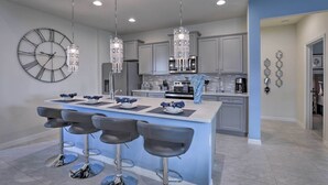 A modern kitchen with a central island, bar stools, pendant lights, and a large wall clock. - 3 Mi to Disney: Family-friendly Home w/ Pool (Kissimmee)