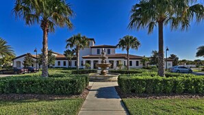 A white building with a fountain in the center, surrounded by palm trees and a well-maintained lawn. - 3 Mi to Disney: Family-friendly Home w/ Pool (Kissimmee)