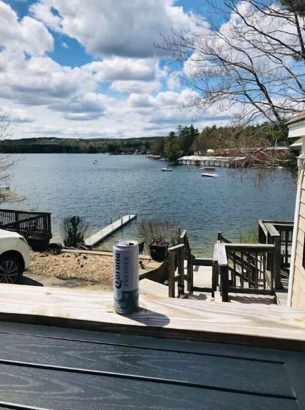 A lakeside view from a deck with a can of Corona beer, dock, and boats.