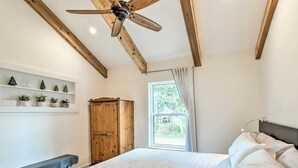 A bedroom with a bed, a wooden wardrobe, a bench, a ceiling fan, and a window with curtains. - Trendy Palm City Cottage w/ Porch on 5 Acres! (Palm City)