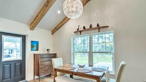 A dining area with a wooden table, two chairs, a chandelier, and a window with a view of trees. - Trendy Palm City Cottage w/ Porch on 5 Acres! (Palm City)