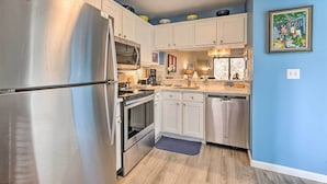 Una cocina compacta con gabinetes blancos, electrodomésticos de acero inoxidable y una pared de acento azul.