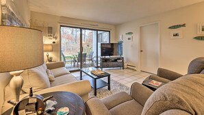 Sala de estar con sofá, mesa de centro y televisor. Posee una puerta corrediza de vidrio que da a un área exterior con una mesa y sillas de patio.