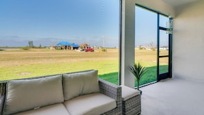 Ein Balkon mit einer Rattan-Couch, einem Blumentopf und Blick auf ein Wiesfeld und Gebäude.