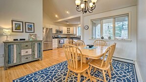 A spacious kitchen with wooden cabinets, a dining table with chairs, and a chandelier. - Spacious Waterfront Falmouth Home on Jenkins Pond! (East Falmouth)