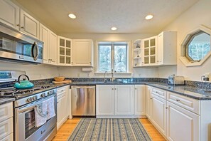 A kitchen with white cabinets, stainless steel appliances, a large window, and a patterned rug.