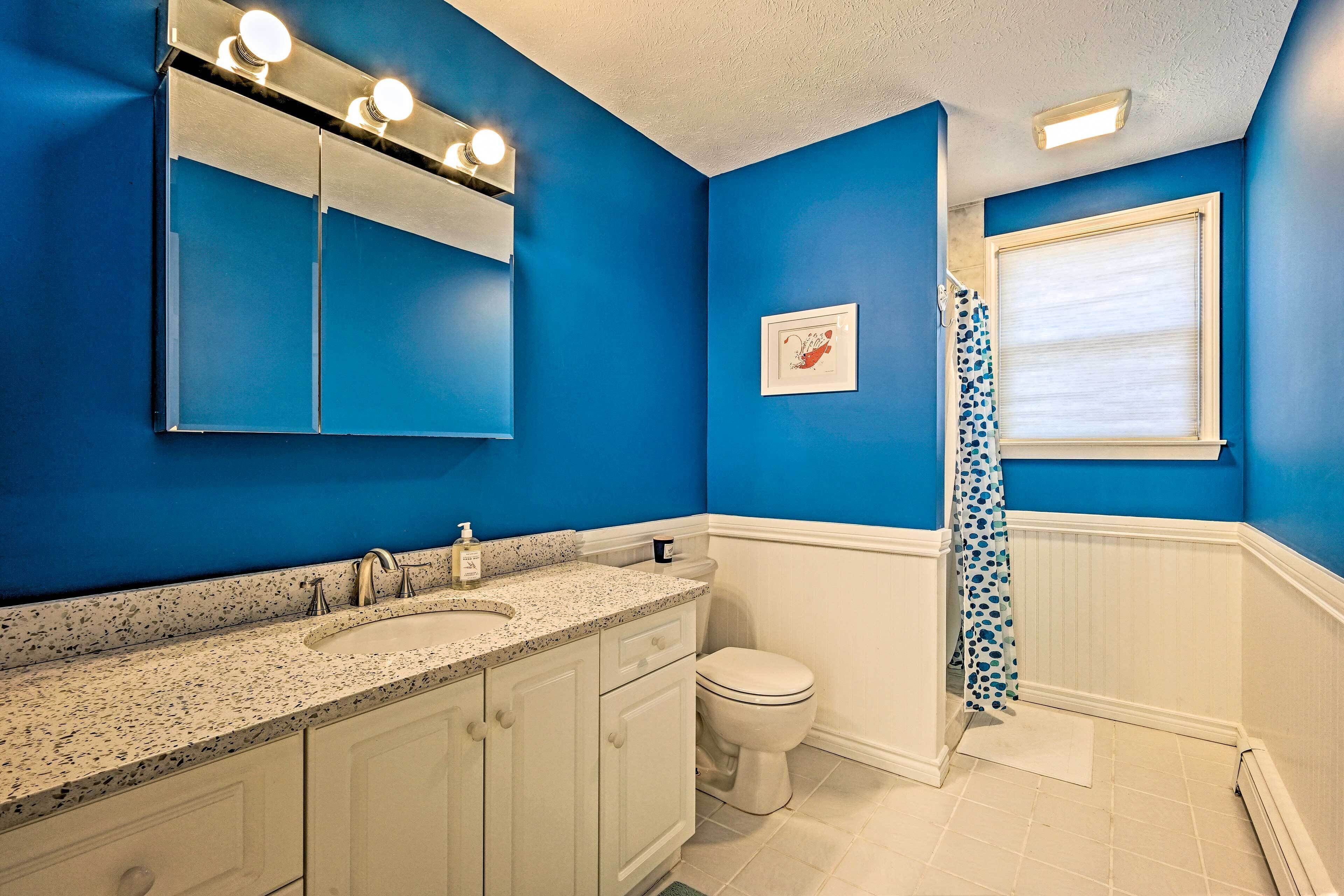 A bathroom with a blue wall, white vanity, and a shower with a blue polka dot curtain.