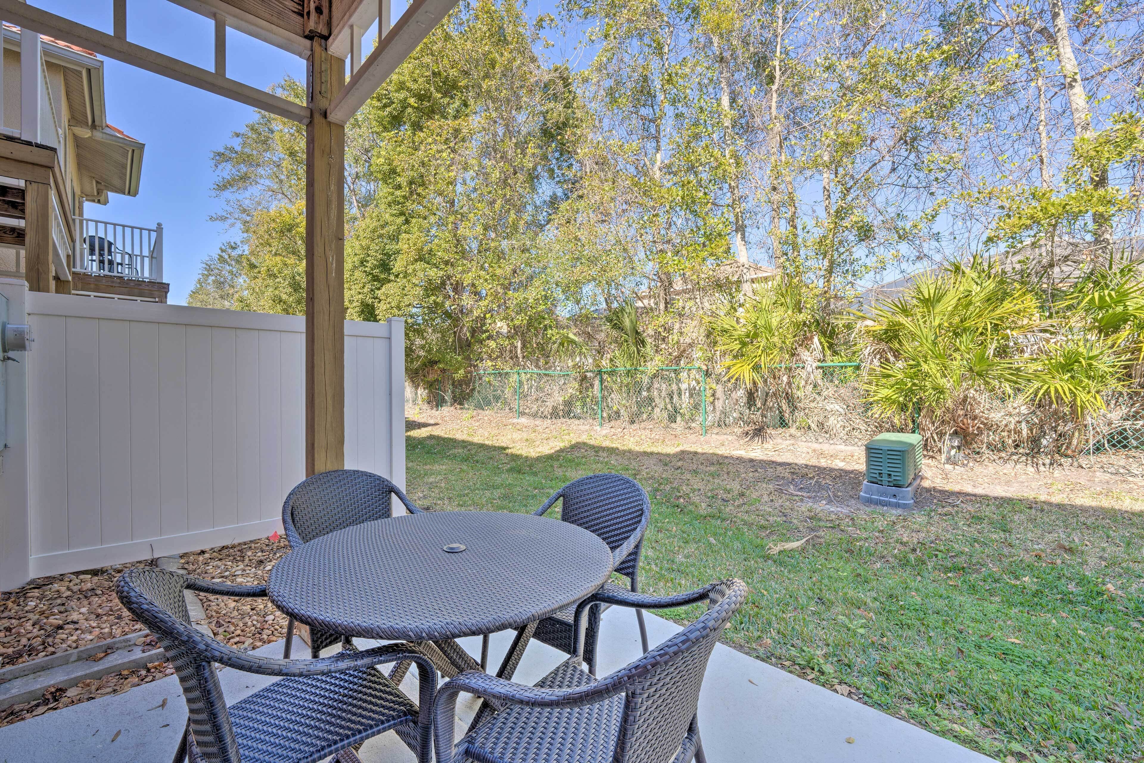 An outdoor patio with wicker furniture, a white fence, and trees in the background.