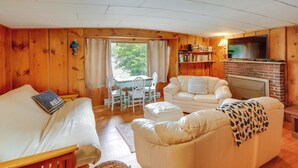 A cozy cabin-style room with a white sofa, a small white table, and a fireplace. - Rustic Berkshires Cottage at Lake Buel w/ Kayaks! (Great Barrington)