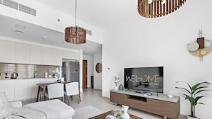 Ein modernes Wohnzimmer mit Flachbildfernseher, eine Essecke mit Tisch und Stühlen sowie eine Küche mit weißen Schränken und Edelstahlgeräten.