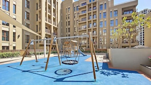 Ein Spielplatz mit Schaukeln und einer Rutsche, umgeben von Mehrfamilienhäusern.