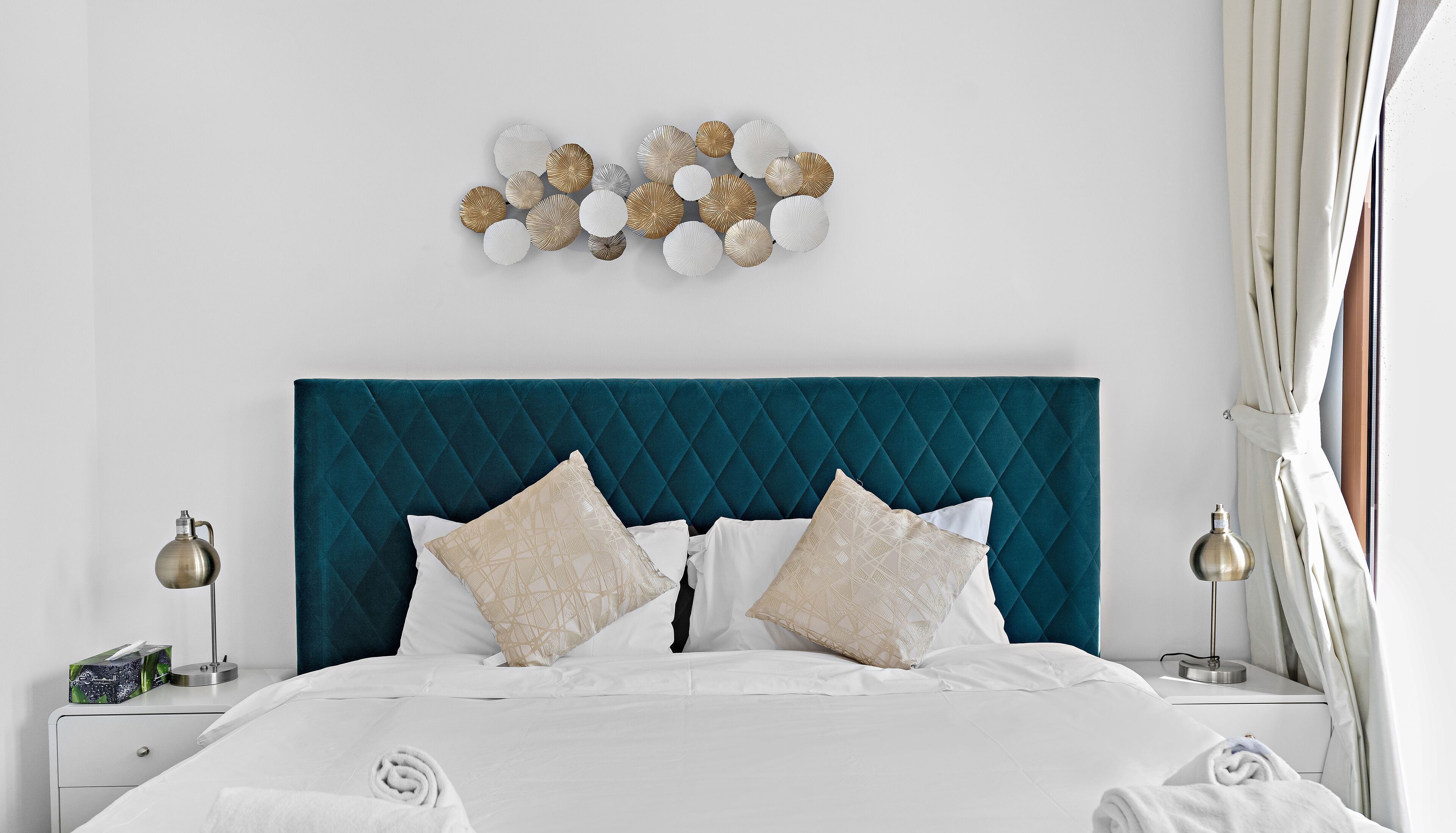 Una cama bien hecha con sábanas blancas, un cabecero acolchado color turquesa y almohadones decorativos.