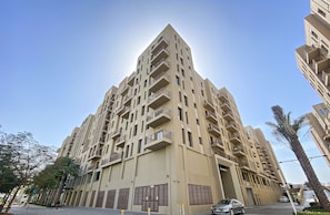 A multi-story residential building with balconies, a gated entrance, and a clear sky.