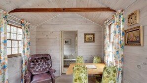 Ein gemütliches Zimmer mit Holzwänden, Holzboden, einem Ledersessel, einem Holztisch, floralen Stühlen und einem Sofa.