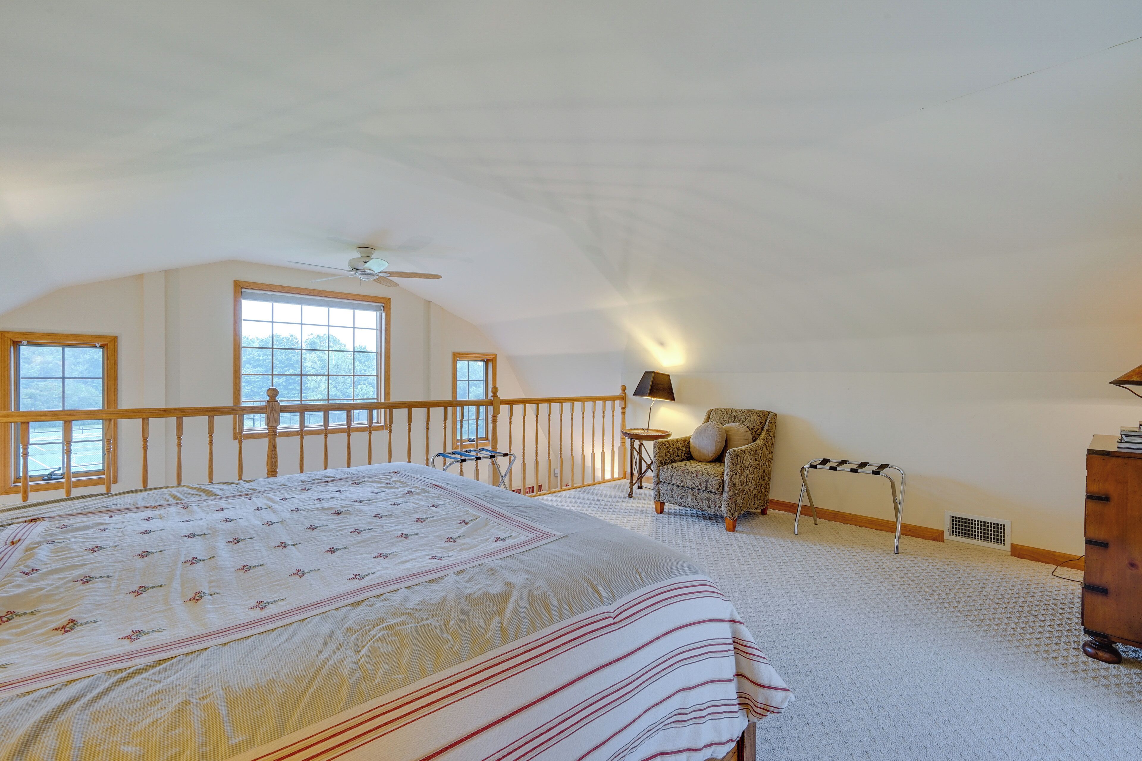 A bedroom with a large bed, a chair, a small table, a lamp, and a view of the outdoors through a window.
