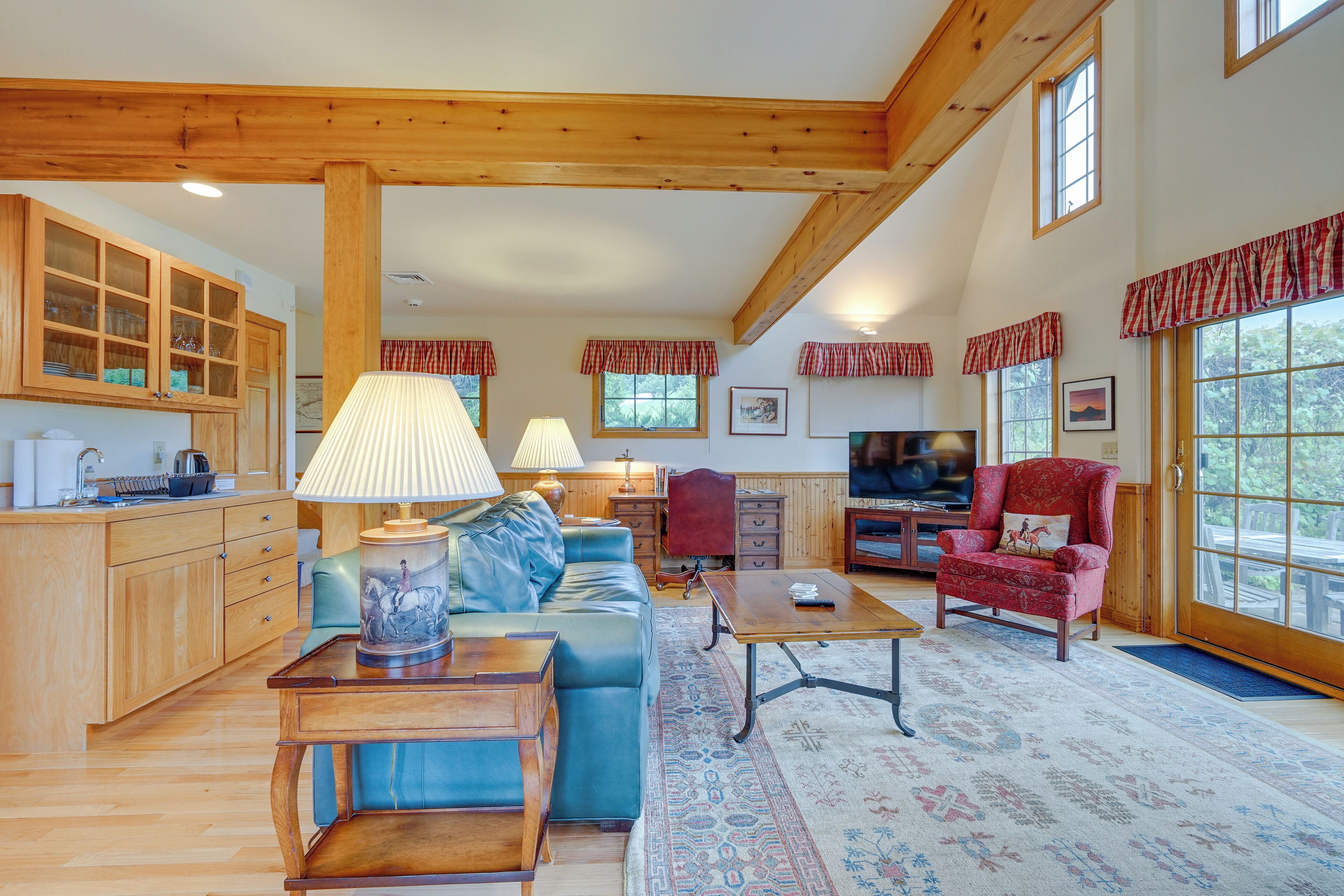 A spacious living room with a wooden ceiling, a blue sofa, a red armchair, a wooden coffee table, and a television.