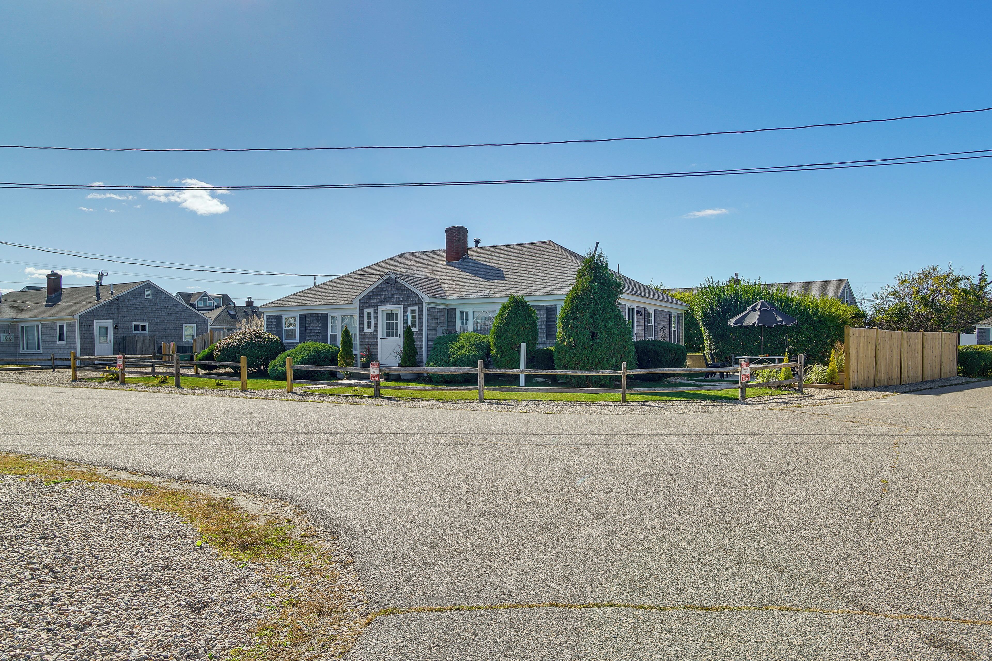 A residential street with houses, a gravel driveway, and a wooden fence.