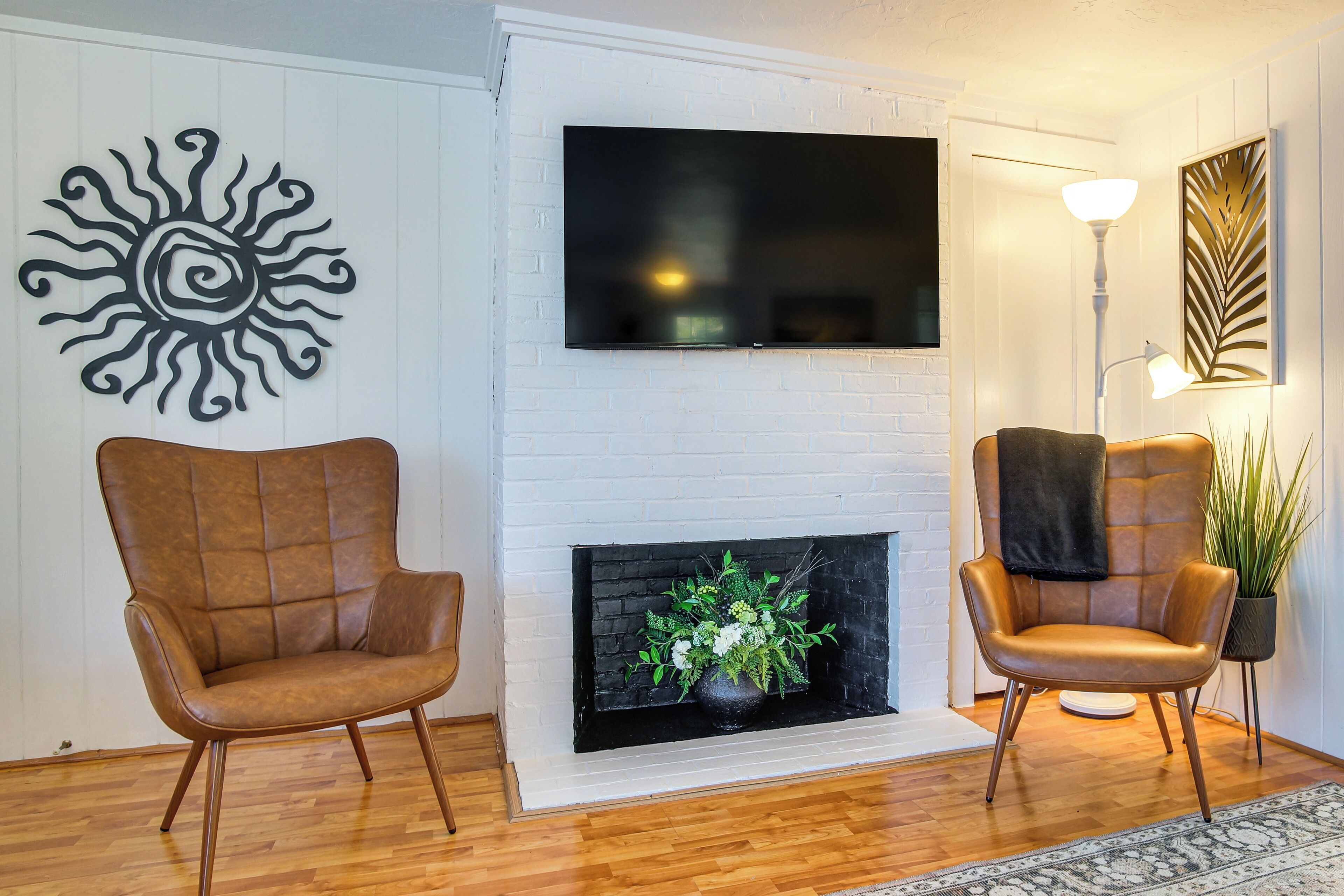 A living room with a fireplace, two leather armchairs, a flat-screen TV, and a decorative sun wall art piece.