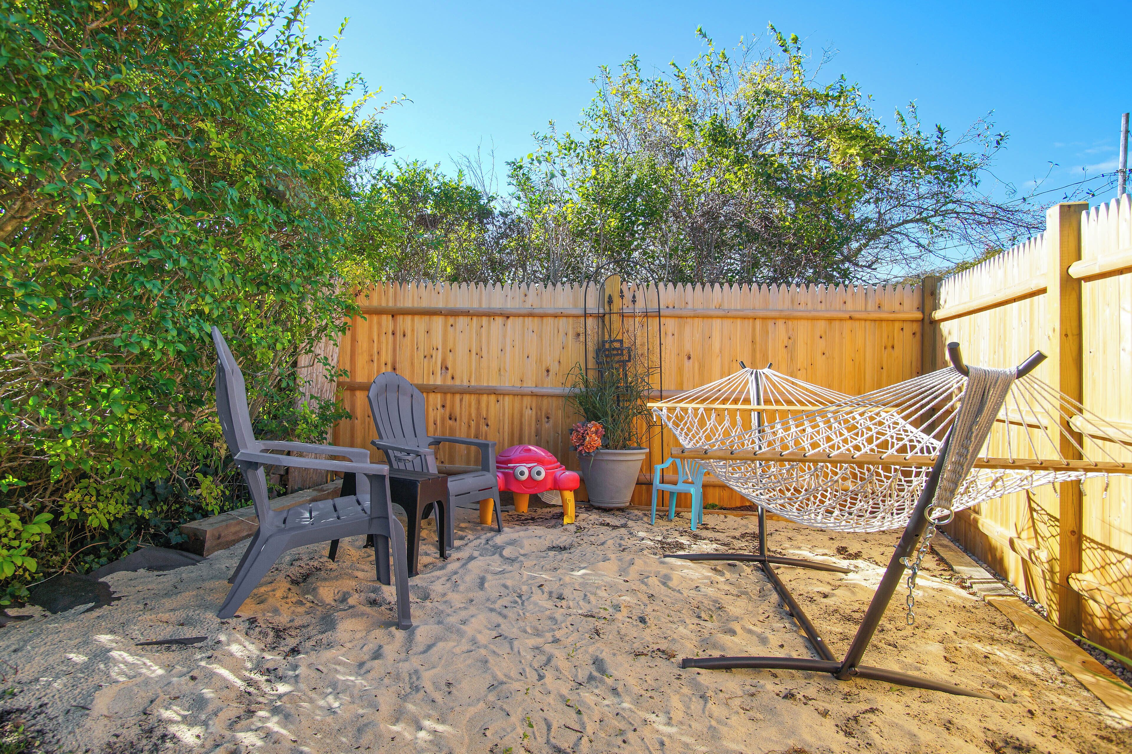 Ein Sandhof mit Holzfence, einer Hängematte und Gartenmöbeln.