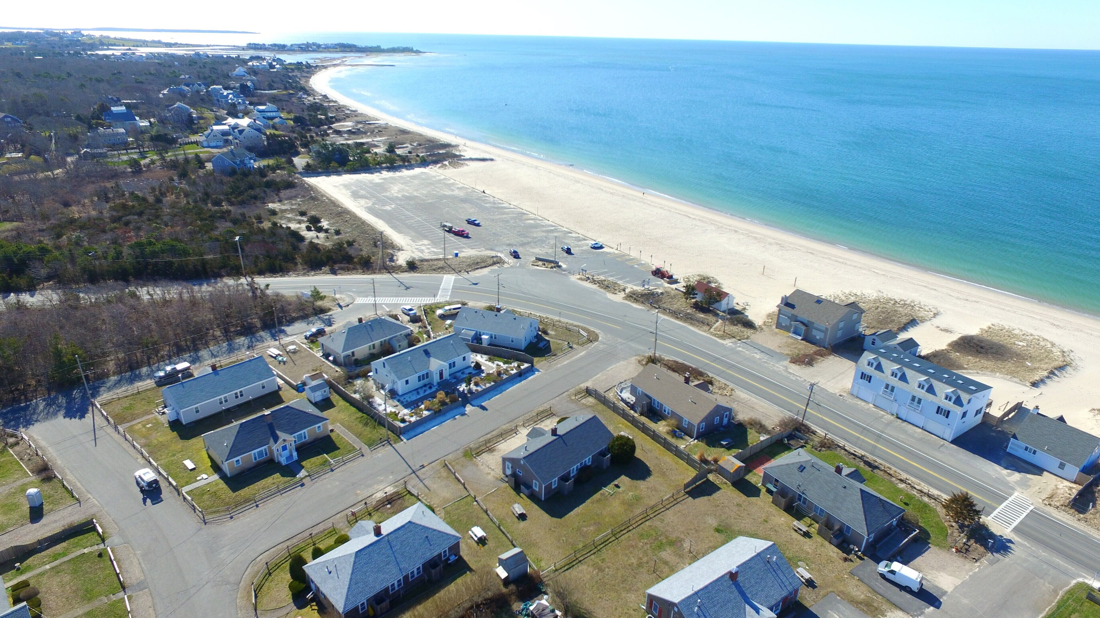 An aerial view of a coastal residential area with houses, a beach, and a road.