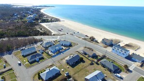 An aerial view of a coastal residential area with houses, a beach, and a road.