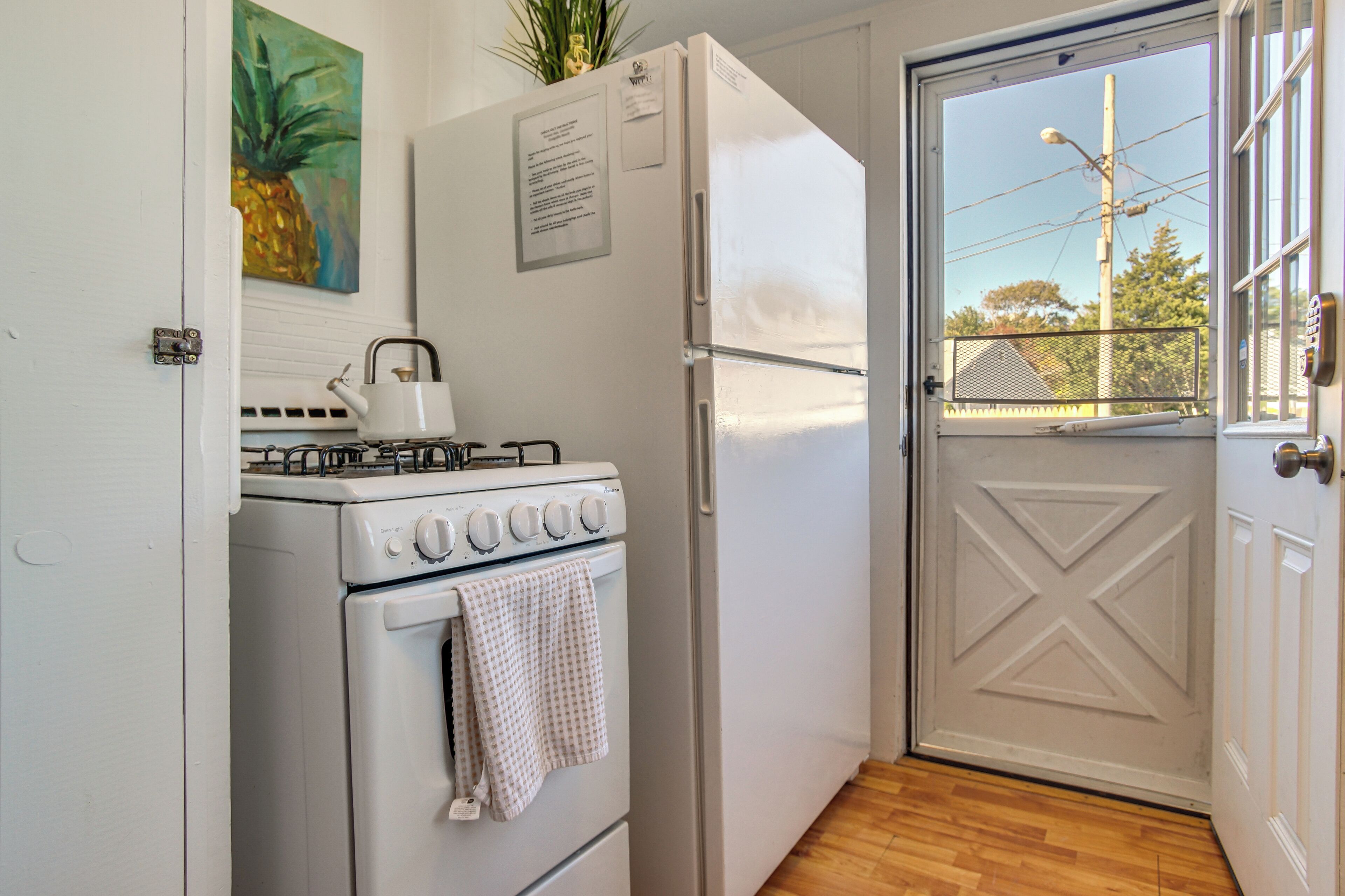 Cozinha compacta com fogão, geladeira e porta que dá para uma varanda com vista para a rua.