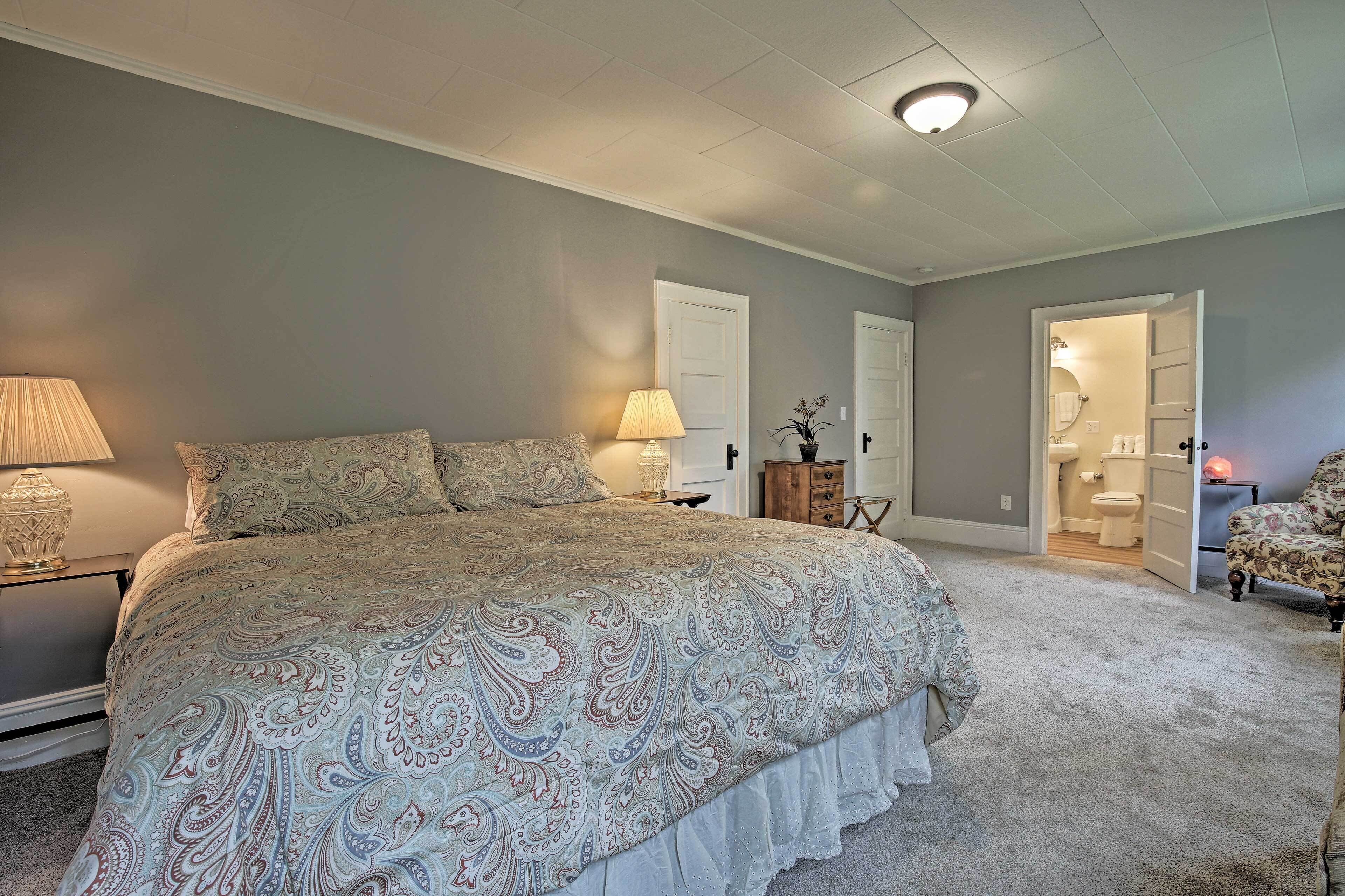A bedroom with a large bed, a bedside table with a lamp, and a door leading to a bathroom.