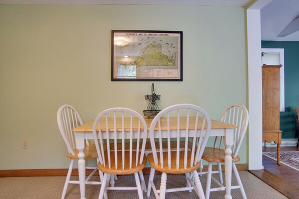 A dining area with a table and four white chairs, a framed map on the wall, and a wooden cabinet in the background.