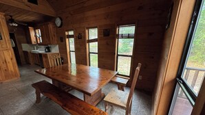 A wooden cabin interior with a large dining table, benches, and a kitchen area. - Cozy waterfront house in quiet neighborhood! (Jasper)