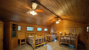 A log cabin bedroom with four wooden beds, a ceiling fan, and a television in a wooden cabinet. - Cozy waterfront house in quiet neighborhood! (Jasper)
