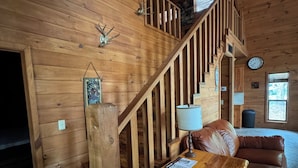 A wooden interior with a staircase, a leather sofa, a table with papers, and a wall clock. - Cozy waterfront house in quiet neighborhood! (Jasper)