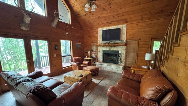 A cozy cabin interior with a stone fireplace, leather sofas, and a television mounted above it. - Cozy waterfront house in quiet neighborhood! (Jasper)