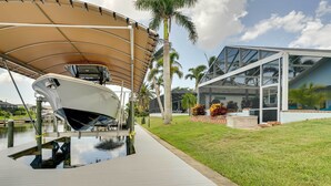 Un barco amarrado bajo un toldo, una estructura con paredes de vidrio y un área verde con palmeras.