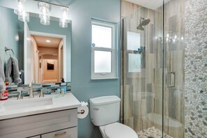 Ein modernes Badezimmer mit einer gläsernen Duschkabine, einer weißen Toilette und einem Waschtisch mit Spiegel und Beleuchtung.