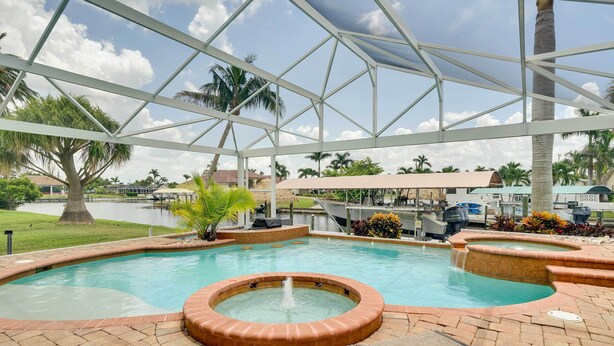 Piscina con jacuzzi, rodeada de palmeras y una zona cubierta con sillones de descanso.