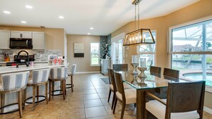 Una cocina moderna con una isla central, taburetes de bar y un comedor con mesa de vidrio y sillas.