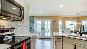 Una cocina moderna con una estufa grande, microondas y horno de puerta de vidrio. Se puede ver un comedor con una mesa y sillas a través de una puerta de vidrio.