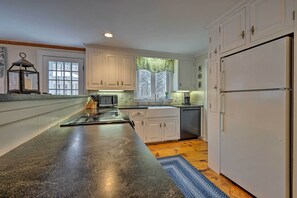 A kitchen with white cabinets, a black countertop, a window with a green valance, and a white refrigerator. - 1 Mi to Nauset Beach: Upscale Orleans Home w/ Deck (Orleans)