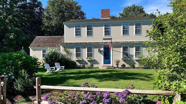 A two-story house with a front porch, a flag, and a well-maintained lawn. - 1 Mi to Nauset Beach: Upscale Orleans Home w/ Deck (Orleans)