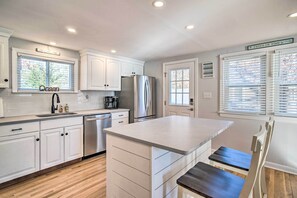 A modern kitchen with white cabinetry, a stainless steel refrigerator, and a built-in island with a bench. - Walk to Great Pond: Spacious East Falmouth Home (East Falmouth)