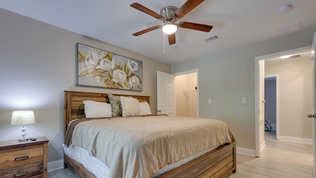 A bedroom with a wooden bed, a ceiling fan, a nightstand, and a painting on the wall. - Dog-friendly Pensacola Duplex ~ 7 Mi to Downtown (Pensacola)