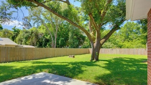 A backyard with a wooden fence, a tree, and a brick house. - Dog-friendly Pensacola Duplex ~ 7 Mi to Downtown (Pensacola)