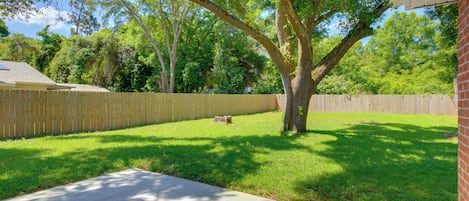 A backyard with a wooden fence, a tree, and a brick house.