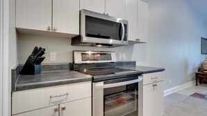 A kitchen with white cabinets, a microwave, an oven, and a countertop with a knife block. - Dog-friendly Pensacola Duplex ~ 7 Mi to Downtown (Pensacola)