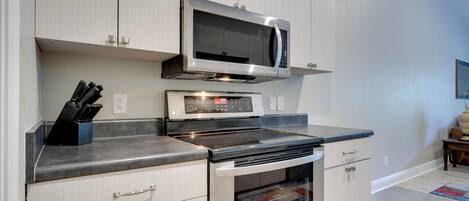 A kitchen with white cabinets, a microwave, an oven, and a countertop with a knife block.