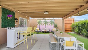 Eine Außenpatio mit Barbereich, Sitzgelegenheiten und einem Wandbild mit Palmen.